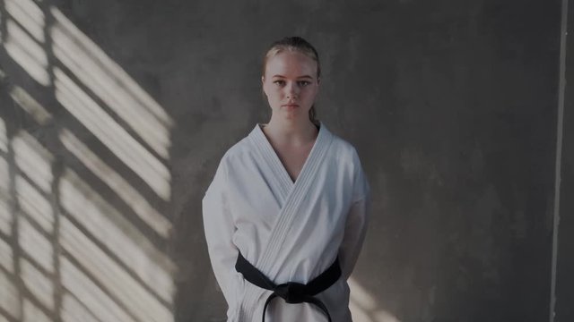 A girl belts a white kimono and looks up at the camera. Serious female fighter ready for action and attack. Taekwondo traditional martial arts. kombat sports.