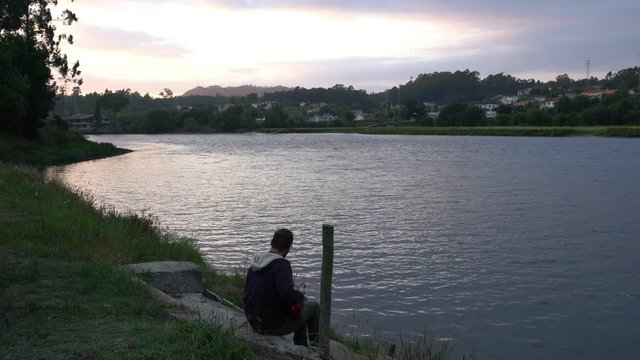 Caucasian man singing and playing with guitar relaxing near a river at sunset