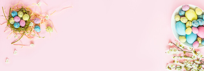 Stylish background with colorful easter eggs isolated on pink pastel background with blooming cherry branches. Horizontal long banner for web design. Flat lay, top view, mockup, overhead, template.