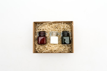 scented candles in colored glass jars in a cardboard box with packaging tinsel. gift on a white background
