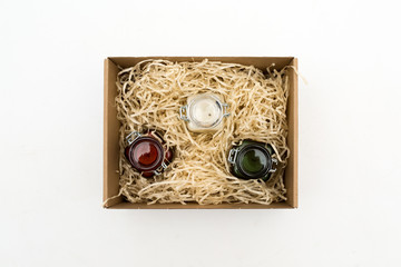 scented candles in colored glass jars in a cardboard box with packaging tinsel. gift on a white background