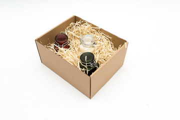 scented candles in colored glass jars in a cardboard box with packaging tinsel. gift on a white background