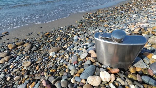 vintage metal hip flask on pebbles on a beach. celebration of men's holiday at sea. conception International Men's Day and Fatherland defender day February 23. copy space