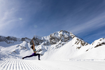 A young woman practice yoga in mountains. With a great view of snow and winter landscape.