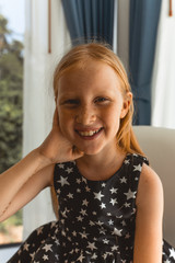 Little girl with red hair shows different emotions. Sadness, joy and happiness. She smiles and cries. In a black dress with skin pigment on her face, freckles