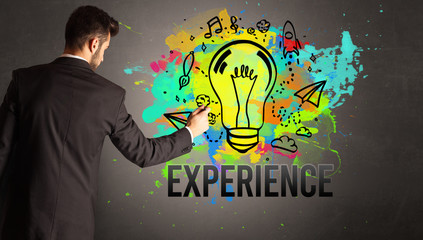 businessman drawing colorful light bulb with EXPERIENCE inscription on textured concrete wall, new...