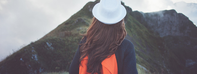 Traveling woman with backpack and white hat looking at mountain at cloudy day
