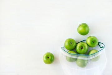 Reusable eco-friendly bag with green apples on a white wooden background. Sustainable lifestyle concept, zero waste shopping, ecological. Top view, flat lay, copy space.