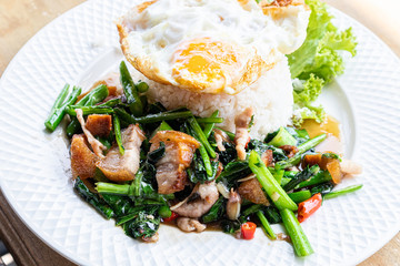 Crispy pork with Chinese kale with steamed rice and fried egg on a white plate.