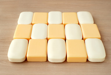 A lot of solid soap on a wooden background. The soap is white and yellow in a square shape. Soap for cleanliness and hygiene. A lot of multi-colored soap.