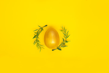 Egg of gold color and green twigs on a plain yellow background. Easter holiday card. Copyspace.