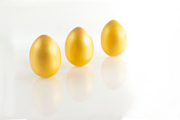 Three eggs of gold color on a white background. Minimalistic composition. Easter holiday card.