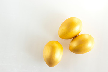 Three eggs of gold color on a white background. Minimalistic composition. Easter holiday card.