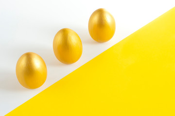 Three eggs of gold color on a white-yellow background. Minimalistic composition. Easter holiday card.