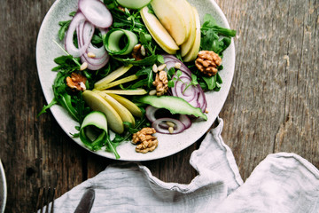 Vegetarian salad of fresh apples with arugula, onions and nuts in a plate on the table
