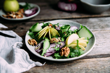 Vegetarian salad of fresh apples with arugula, onions and nuts in a plate on the table