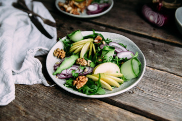 Vegetarian salad of fresh apples with arugula, onions and nuts in a plate on the table