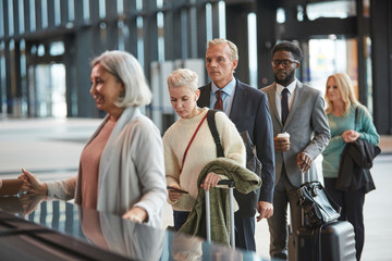Group of people standing in queue at airport check-in counter desk, horizontal medium shot, copy space