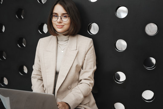 Close-up porrait of young elegant woman, university student searching career opportunities in internet, holding computer on laps as studying at co-working space on floor, smiling camera