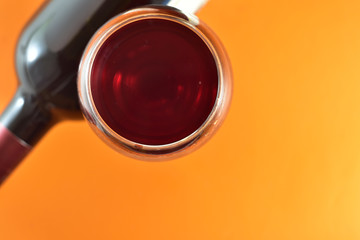 Glass and bottle of red wine on an orange background