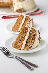 Close up of two pieces of cake with cream cheese frosting ready for eating with the cake in behind.
