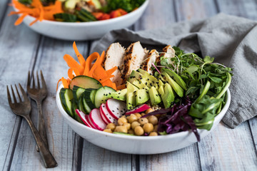 Close up view of a buddha bowl with fresh vegetables, chickpeas and grilled chicken ready for eating.
