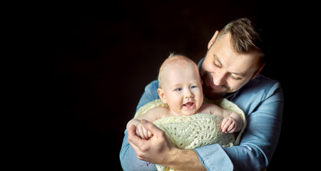 A happy father lives in the arms of a newborn baby, hugs and poses creamly. Paternity