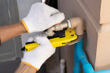 Plumber man hand using pvc pipe cutter for cut the water pipe at home. Maintenance concept.