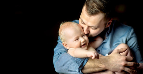 A happy father lives on the hands of a newborn baby, hugs and kisses creamly. Paternity