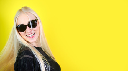 Portrait of a happy blonde girl smiling and posing on a yellow background.