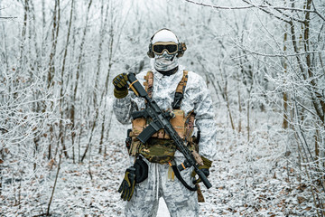 Military man in white camouflage uniform with machinegun. Soldier in the winter forest territory...