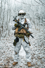 Military man in white camouflage uniform with machinegun. Soldier in the winter forest territory...