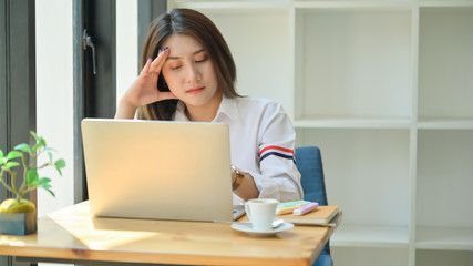 A young woman looks tired using a laptop. She is serious about research to graduate.