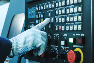 A gloved operator’s hand presses a button on the CNC control panel of the machine