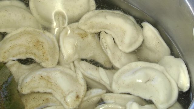 A woman puts dumplings in boiling water. Pelmeni in boiling water. Closeup of metal stewpan with boiling water and dumplings. Home cooking. Boiling water rises steam.