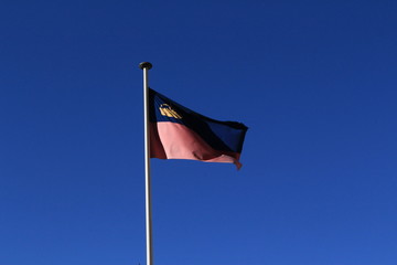 Real Liechtenstein national flag fluttering on a flag pole in wind, isolated on real blue sky background.