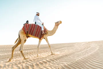 Foto auf Glas Man wearing traditional clothes, taking a camel out on the desert sand, in Dubai © oneinchpunch