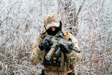 Airsoft man in camouflage uniform and machinegun with optical sight. Soldier in the winter forest. Horizontal photo side view.