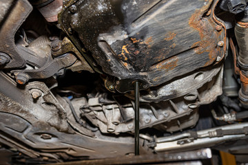 Draining used diesel engine oil from an oil pan into a metal container in a car workshop.