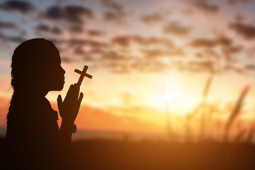 Silhouette of little girl holding christian cross in hands to praying for blessing from god at sunset background.