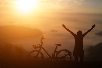 Silhouette of man raised his hand with a bike against sunset background.