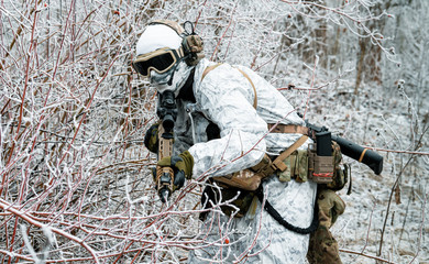 Military man in white camouflage uniform with machinegun. Soldier sneaking in the winter forest...