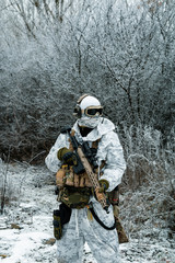 Fototapeta premium Military man in white camouflage uniform with machinegun. Soldier in the winter forest territory background