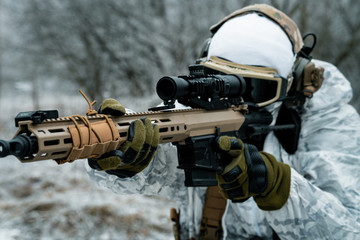 Closeup military man in white camouflage uniform with machinegun. Soldier aims of the machinegun