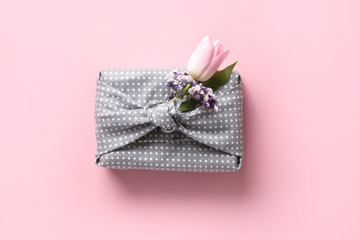 Spring eco-friendly gift wrapped in grey textile with flowers decor on pink. Sustainable gift. Zero waste. Easter holiday. Traditional Japanese Furoshiki style. View from above.