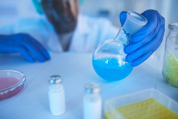 Horizontal close up shot of unrecognizable male laboratory worker looking at blue liquid in glass flask, copy space
