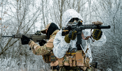 Two men in camouflage white, green uniform with machineguns back to back. Soldiers with muchinegun in the winter forest. Horizontal photo, side view. © Bohdan Petrushko
