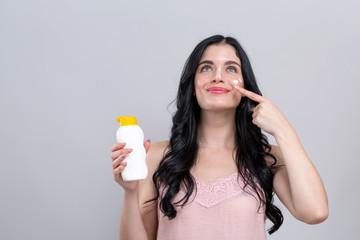 Young woman with sunscreen on a gray background