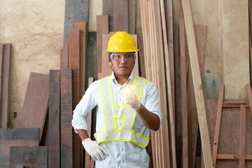 Handsome man wearing protective glasses and yellow helmet,raise blurred left hands up with determind eyes,standing in front of wood pile,at factory