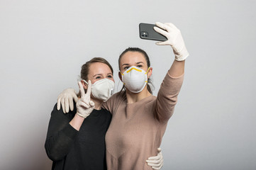 Frauen mit Mundschutz Maske und Schutzandschuhen tippen auf dem Mobiltelefon, machen Selfies und...